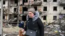 Seorang wanita berjalan di depan bangunan yang rusak setelah peluru militer Rusia menghantam di Koshytsa Street, Kiev, Ukraina (25/2/2022). Ledakan di Kiev memicu kekerasan setelah Presiden Rusia Vladimir Putin menentang peringatan Barat untuk melancarkan invasi darat skala penuh. (AFP/Daniel Leal)