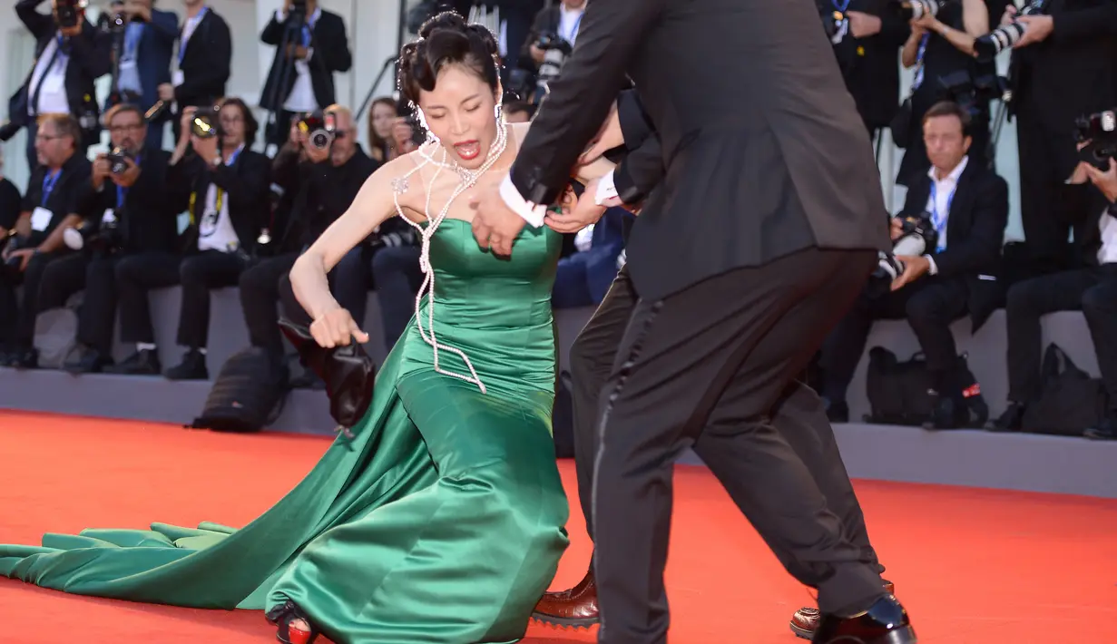 Aktris Korsel Moon So-ri kehilangan keseimbangan usai sepatu hak tingginya menginjak bagian bawah gaun yang panjang menjuntai di karpet merah pemutaran perdana film The Light Between Two Ocean di Venice Film Festival, Kamis (1/9). (FILIPPO MONTEFORTE/AFP)