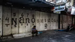 Seorang pria duduk di di depan pertokoan kawasan perdagangan Pasar Baru yang tutup, Jakarta, Jumat (3/4/2020). Sebagian pemilik toko di Pasar Baru memilih menutup usahanya sementara waktu untuk mengantisipasi meluasnya penyebaran virus corona COVID-19. (Liputan6.com/Faizal Fanani)