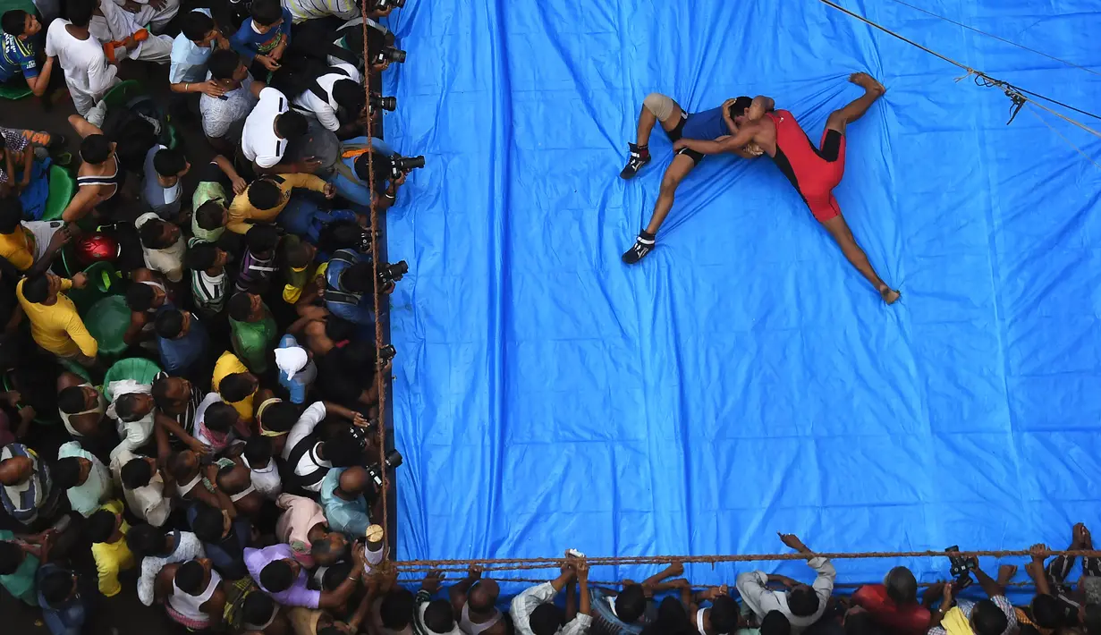 Sejumlah penonton memadati ring, saat pegulat bertarung di Kolkata, India (18/10). Pertandingan gulat ini digelar di tengah jalan yang padat di daerah Kolkata. (AFP Photo/Dibyangshu Sarkar)