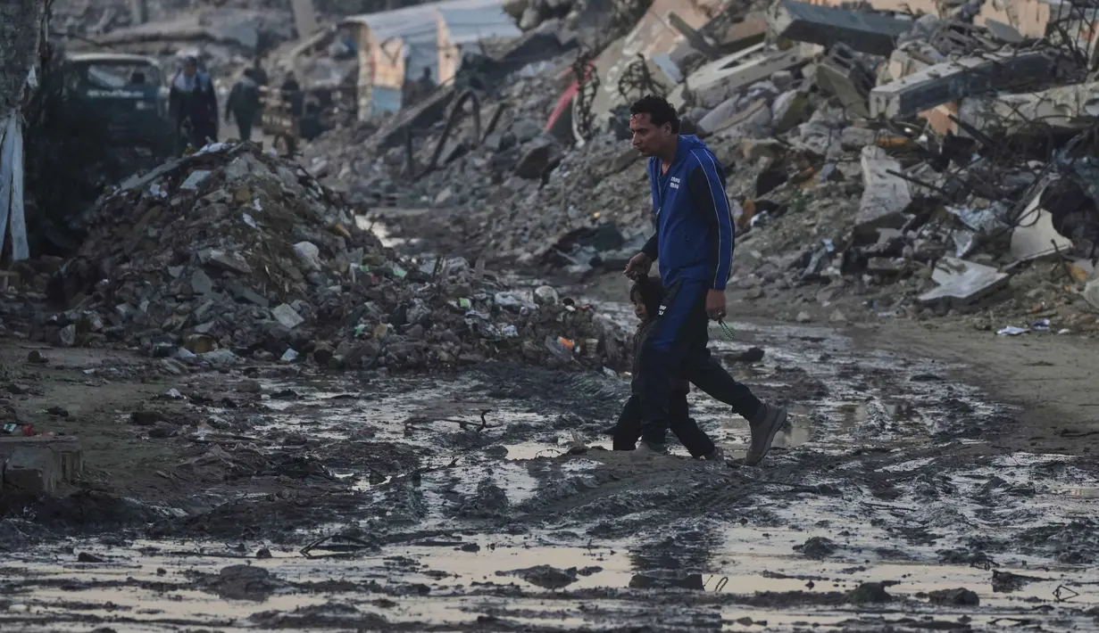 Warga Palestina berjalan di tengah bangunan yang hancur akibat serangan udara dan darat Israel di Kota Gaza, Selasa 6 Januari 2026. Komite Internasional Palang Merah (ICRC) terus berupaya menyalurkan bantuan ke Gaza. (AP Photo/Jehad Alshrafi)
