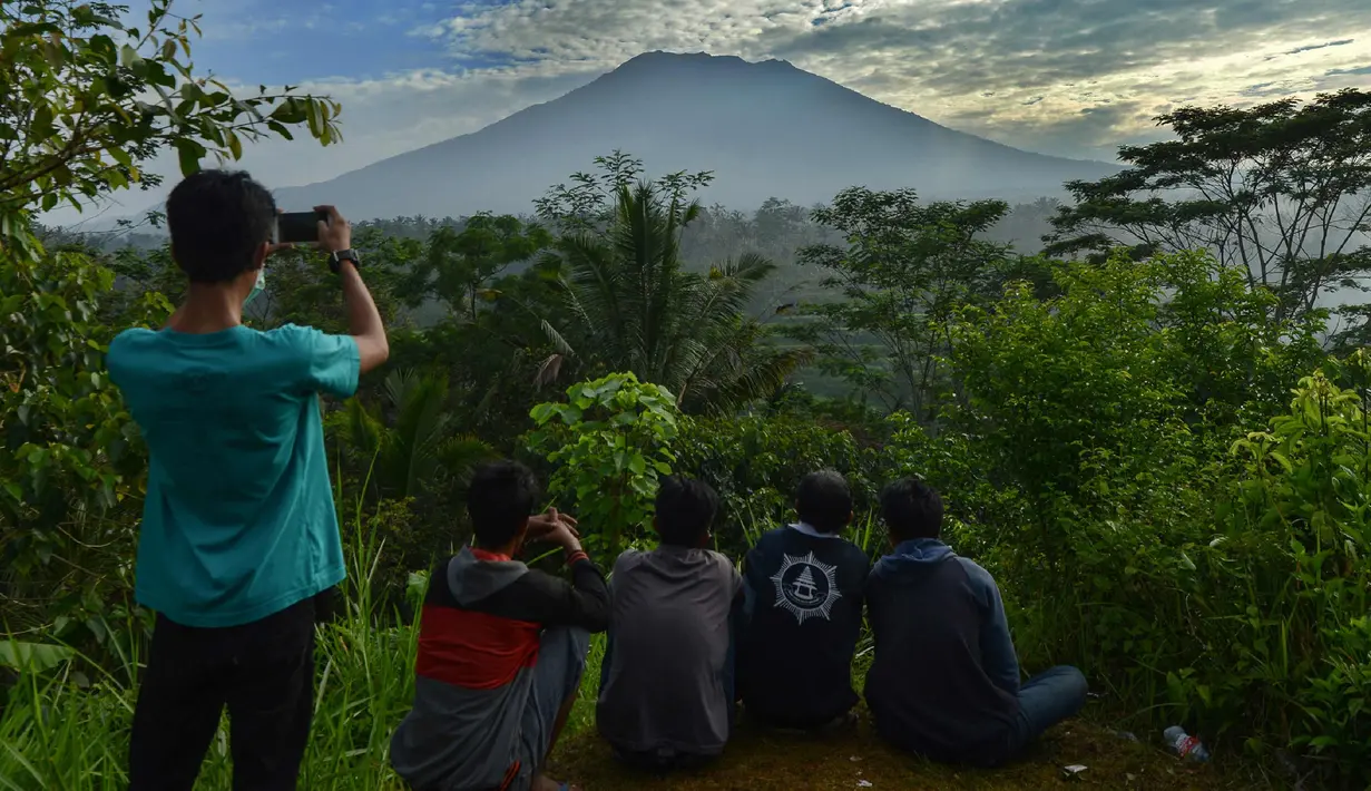 Warga melihat Gunung Agung di Karangasem di pulau resor Bali, Indonesia (24/9). Gunung Agung adalah gunung berapi yang besar dengan puncak 3.142 meter di atas permukaan laut. Gunung ini mendominasi pemandangan timur Bali. (AFP Photo/Sonny Tumbelaka)