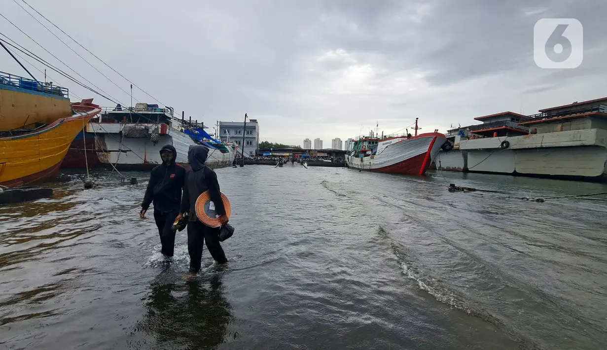 Nelayan melintasi banjir rob saat cuaca ekstrem di Pelabuhan Muara Baru, Penjaringan, Jakarta Utara, Rabu (28/12/2022). Banjir ROB, hujan deras dan  cuaca buruk melanda kawasan Pelabuhan Muara Baru saat siang menjelang sore hari. (Liputan6.com/Johan Tallo)