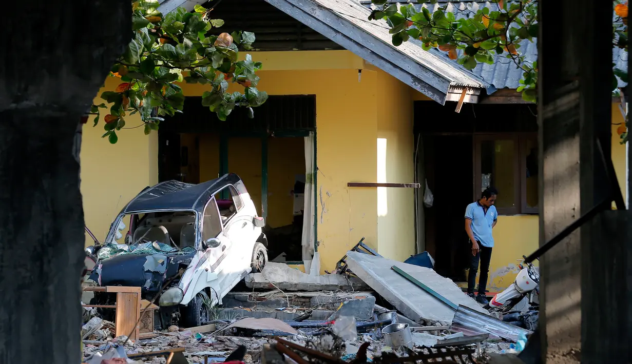 Seorang pria berada di samping mobil yang ringsek sambil memeriksa rumahnya yang rusak setelah gempa dan tsunami di pantai Talise di Palu, Sulawesi Tengah (1/10). (AP Photo/Tatan Syuflana)