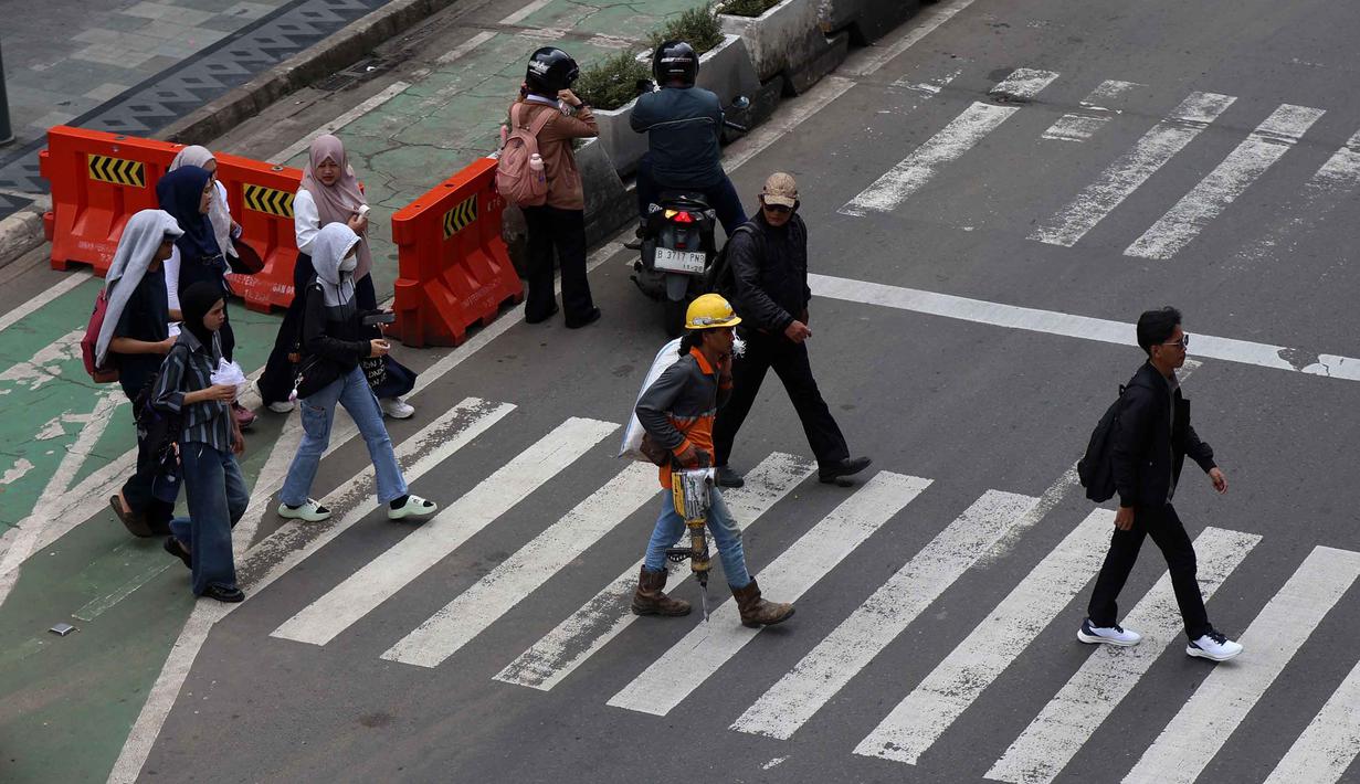 Untuk keamanan, pagar kerja dipasang pada area trotoar, lajur sepeda, dan sebagian badan jalan. Tampak dalam foto, warga melintas di area pedestrian kawasan Jalan MH Thamrin, Jakarta, Senin 20 April 2026. (Kapanlagi.com/Budy Santoso)