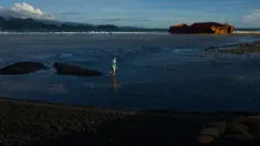 Seorang pria berjalan di pantai Lhoknga yang tercemar tumpahan batu bara dari sebuah tongkang di Aceh, Rabu (1/8). Sekitar 7.000 ton batu bara tumpah dari kapal tongkang yang kandas dihantam gelombang sehingga mencemari pantai. (AFP/CHAIDEER MAHYUDDIN)