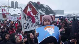 Mereka menolak ancaman aneksasi pulau Arktik tersebut. Tampak dalam foto, seorang anak laki-laki memegang peta Greenland yang dicoret dan dihiasi dengan wig yang melambangkan Presiden AS Donald Trump, selama unjuk rasa di depan konsulat AS di Nuuk, Sabtu 17 Januari 2026. (AP Photo/Evgeniy Maloletka)