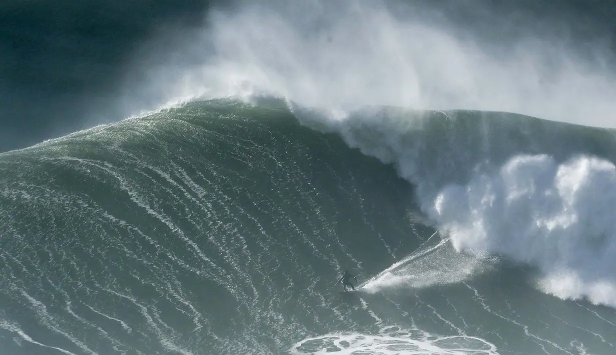 Seorang peselancar menunggangi ombak selama sesi selancar derek di Praia do Norte di Nazare, Portugal (29/10/2020). Gelombang besar, yang ditimbulkan oleh Badai Epsilon di Atlantik Utara, mencapai Portugis pantai barat menarik peselancar ombak besar ke Nazare. (AP Photo/Pedro Rocha)