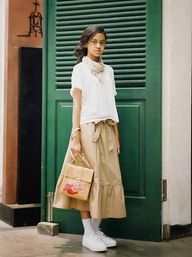 Mengenakan rok dengan aksen pita warna beige jadi pilihan tepat.