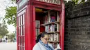 Seorang wanita membaca buku di dekat kotak telepon merah yang telah berubah menjadi perpustakaan pertukaran buku di Lewisham Way, London (21/10). Kotak telepon ini diubah menjadi perpustakaan, kios, hingga tempat reparasi ponsel. (AFP Photo/Tolga Akmen)