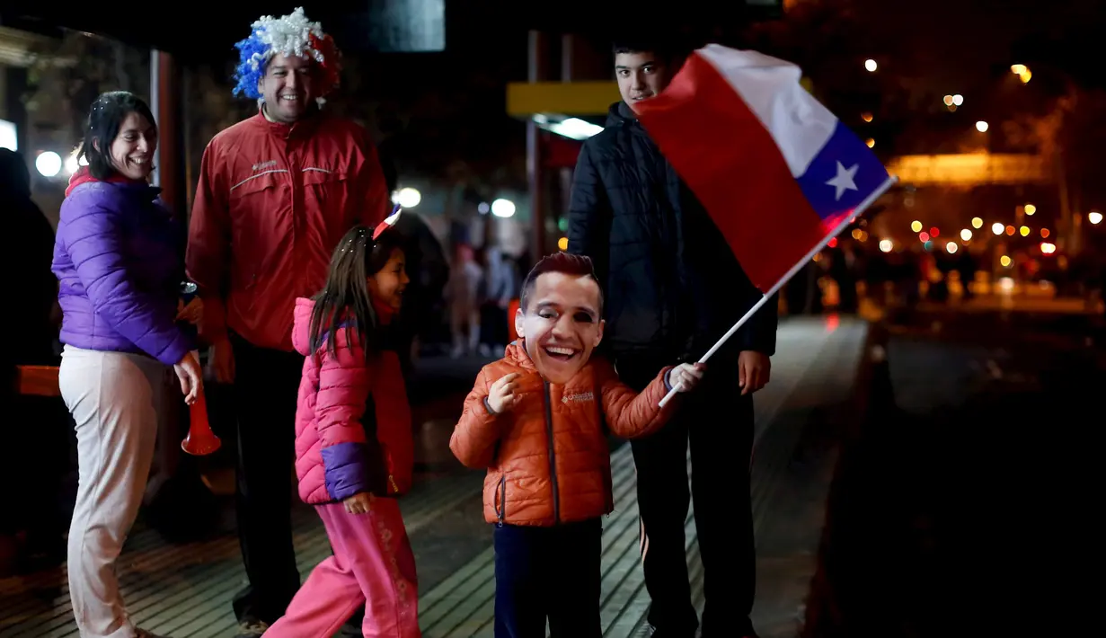 Seorang anak membawa bendera Chile sambil memakai topeng penyerang Chile, Alexis Sanchez merayakan kemenangan Chile di Copa America 2015 di Santiago, Chile, (25/6/2015). Chile melaju ke semifinal usai mengalahkan Uruguay 1-0. (REUTERS/Pablo Sanhueza)