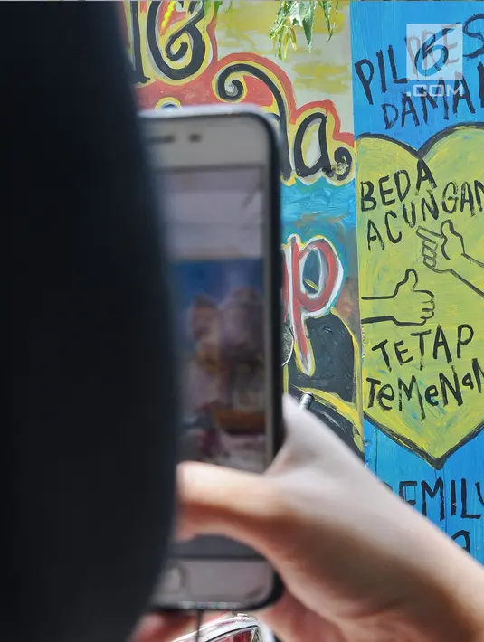 Warga mengambil gambar mural pemilu di Jalan Karet, Depok, Jawa Barat, Rabu (20/3). Mural tersebut mengajak masyarakat untuk berpartisipasi dalam menyukseskan pemilu dengan cara damai dan menjaga meski berbeda pilihan. (Liputan6.com/Herman Zakharia)