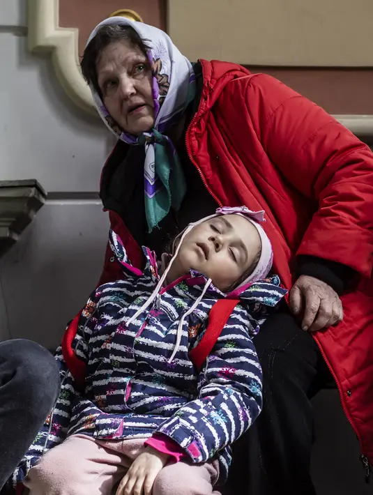 Seorang anak, Sofia tidur di sebelah neneknya Halina saat menunggu kereta mereka menuju Szczecin, di stasiun kereta api di Przemysl, Polandia tenggara, pada 5 April 2022. Lebih dari 4,2 juta pengungsi Ukraina telah meninggalkan negara itu sejak invasi Rusia, kata PBB. (Wojtek RADWANSKI / AFP)