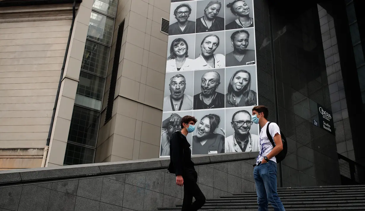 Sejumlah orang berbincang di sebelah potret para petugas kesehatan yang ditempelkan di bagian depan Bastille Opera di Paris, Prancis, Jumat (10/7/2020). Potret hitam putih itu untuk memberi penghormatan kepada pekerja medis yang berjuang menghadapi Corona Covid-19. (AP Photo/Francois Mori)