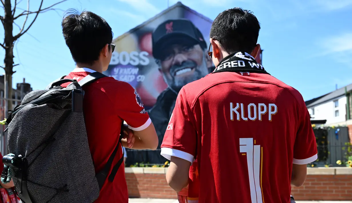 Fans berhenti untuk melihat mural manajer Liverpool Jurgen Klopp karya seniman Hugh Whitaker dari MurWalls di dekat stadion saat mereka tiba untuk menyaksikan laga pekan ke-38 Premier League melawan Wolverhampton Wanderers di Stadion Anfield, Minggu (19/5/2024). (Paul ELLIS / AFP)