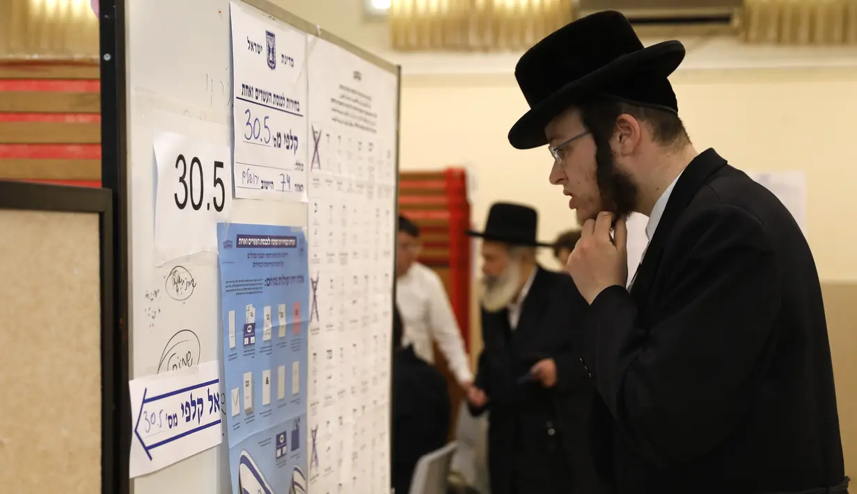 Pria Yahudi ultra-Ortodoks melihat daftar kandidat sebelum memberikan suaranya selama pemilihan parlemen Israel di Yerusalem (9/4). Warga Israel hari ini memberikan suara dalam pemilihan tingkat tinggi yang akan memutuskan masa jabatan PM Benjamin Netanyahu. (AFP Photo/Menahem Kahana)
