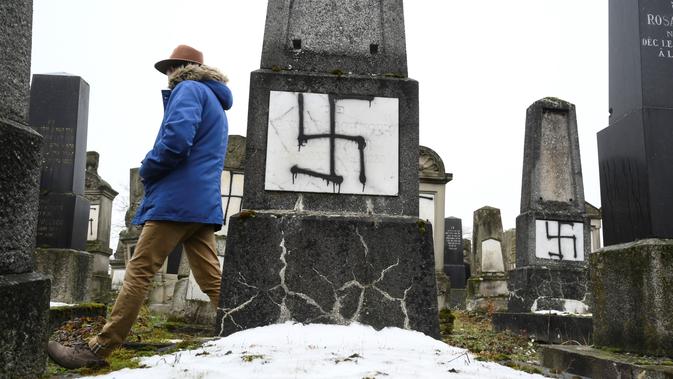 Seorang pria melihat batu nisan yang dicoret-coret lambang swastika nazi di pemakaman Yahudi di Strasbourg, Prancis (17/12). Pihak berwenang belum mengatakan apakah ada hubungan antara aksi vandalisme dengan serangan tersebut. (AFP Photo/Sebastien Bozon)