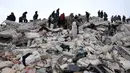 Warga dan tim penyelamat mencari korban dan orang yang selamat di antara puing-puing bangunan yang runtuh setelah gempa bumi di desa Besnaya, provinsi Idlib Barat Laut Suriah perbatasan dengan Turki, pada Senin 6 Februari 2022. Tim penyelamat di Turki dan Suriah menerjang cuaca yang sangat dingin, gempa susulan, dan bangunan yang runtuh, saat mereka menggali korban yang tertimbun oleh gempa bumi yang menewaskan lebih dari 5.000 orang. (OMAR HAJ KADOUR/AFP)