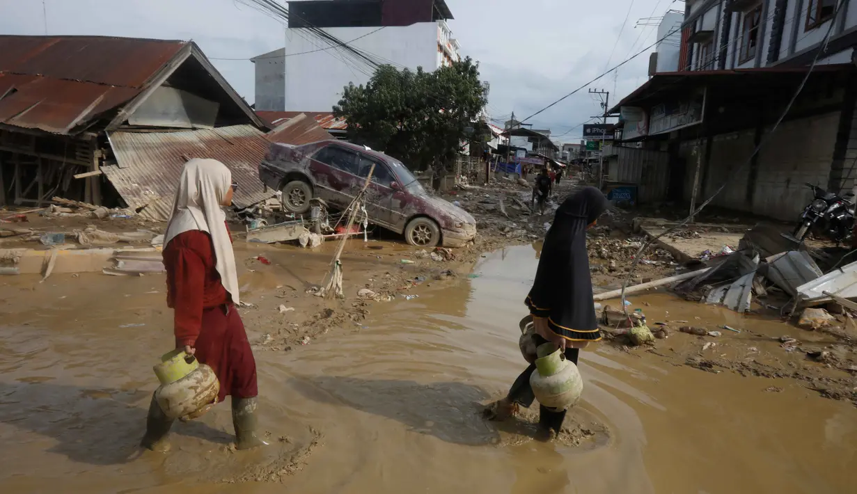 Hingga Kamis (5/12/2025) malam, listrik belum menyala, sehingga jalanan masih gelap gulita. Tampak dalam foto, para penyintas berjalan melewati reruntuhan mobil di area terdampak banjir bandang di Aceh Tamiang, Sumatera, Indonesia, Kamis 4 Desember 2025. (AP Photo/Binsar Bakkara)