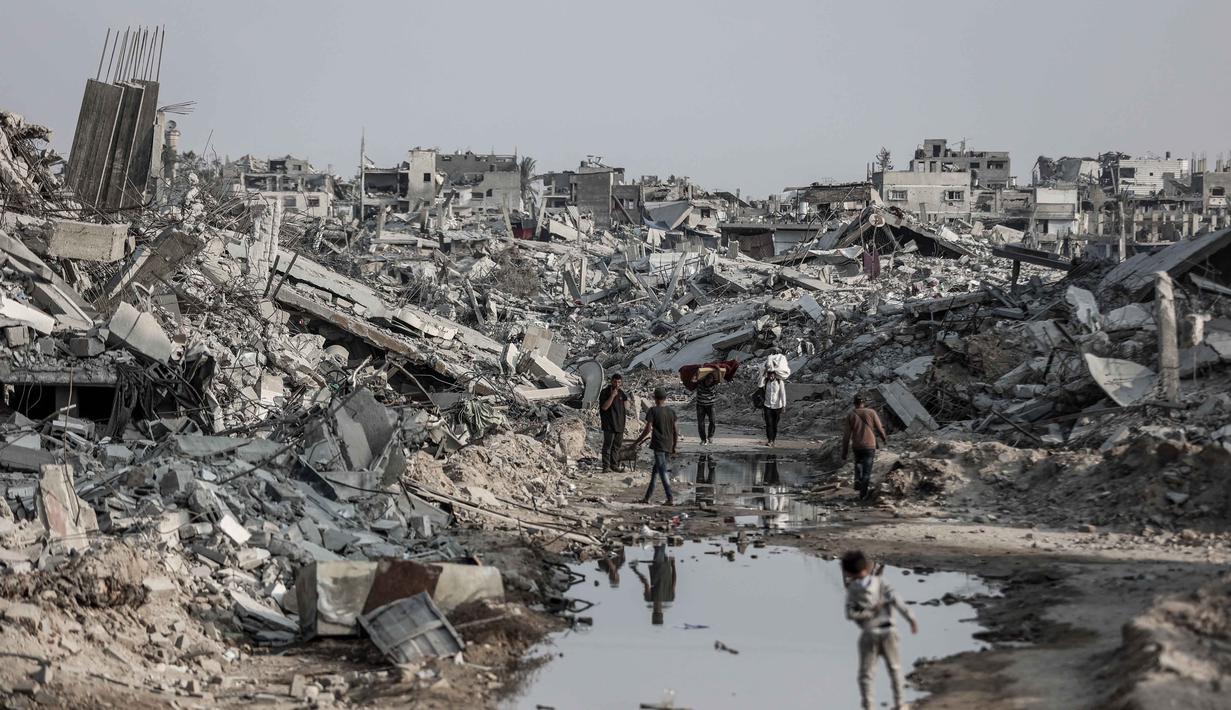 PBB memperingatkan bahwa jumlah tersebut masih jauh dari cukup untuk memenuhi kebutuhan mendesak seluruh warga Gaza. Tampak dalam foto, warga Palestina berjalan melalui puing-puing bangunan yang hancur di Jabalia, di bagian utara Jalur Gaza, pada Jumat 7 November 2025. (Omar AL-QATTAA/AFP)