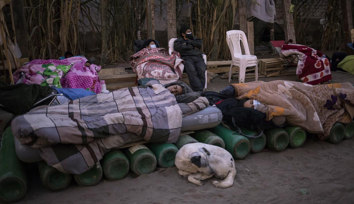 Orang-orang tidur di atas tabung oksigen kosong saat menunggu toko buka untuk mengisi tabung mereka di Villa El Salvador, Lima, Peru, Selasa (6/4/2021). Warga Peru terus berjuang mendapatkan oksigen medis untuk merawat pasien COVID-19. (AP Photo/Rodrigo Abd)