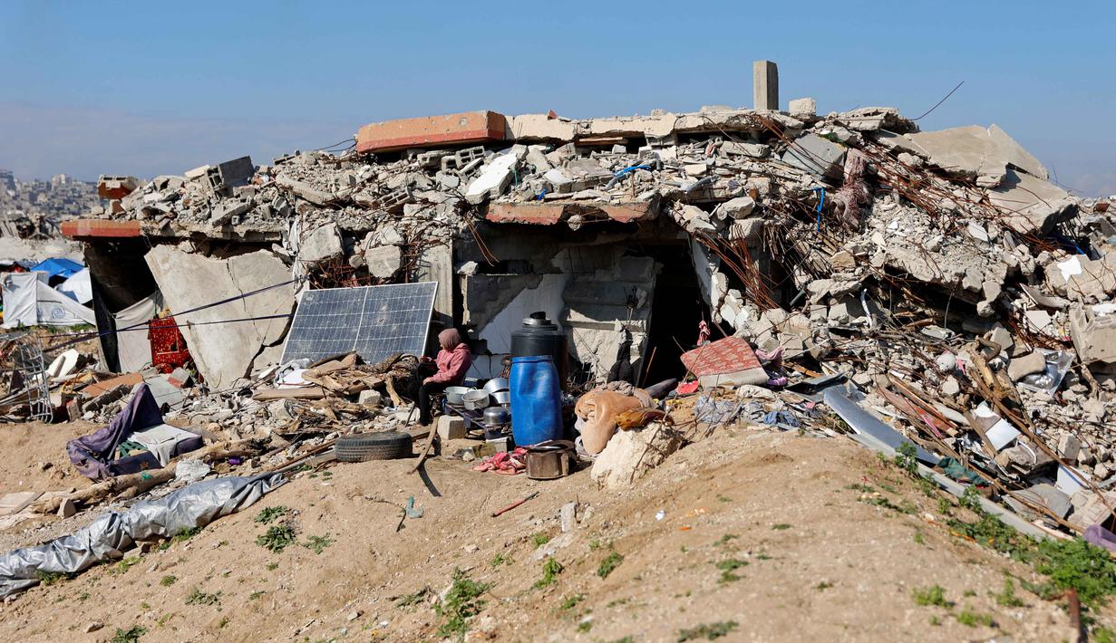 Menurut Trump, Dewan Perdamaian Gaza dirancang untuk mengawasi pembentukan pemerintahan teknokrat Palestina yang masih akan dibentuk, sekaligus memantau proses rekonstruksi di Jalur Gaza. Tampak dalam foto, para pengungsi Palestina hidup di tengah reruntuhan rumah dan bangunan yang hancur akibat serangan militer Israel selama lebih dari dua tahun di wilayah Gaza, di kamp pengungsi Jabalia, di bagian utara Jalur Gaza pada Sabtu 17 Januari 2026. (Omar AL-QATTAA/AFP)
