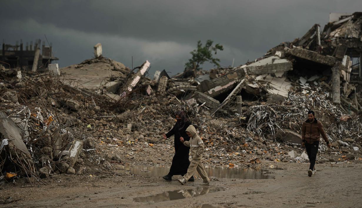 Warga Palestina berjalan melewati reruntuhan di tengah cuaca buruk Kota Gaza, Kamis 11 Desember 2025. Bencana baru mengancam ratusan ribu warga Palestina yang mengungsi di Jalur Gaza. (AP Photo/Jehad Alshrafi)