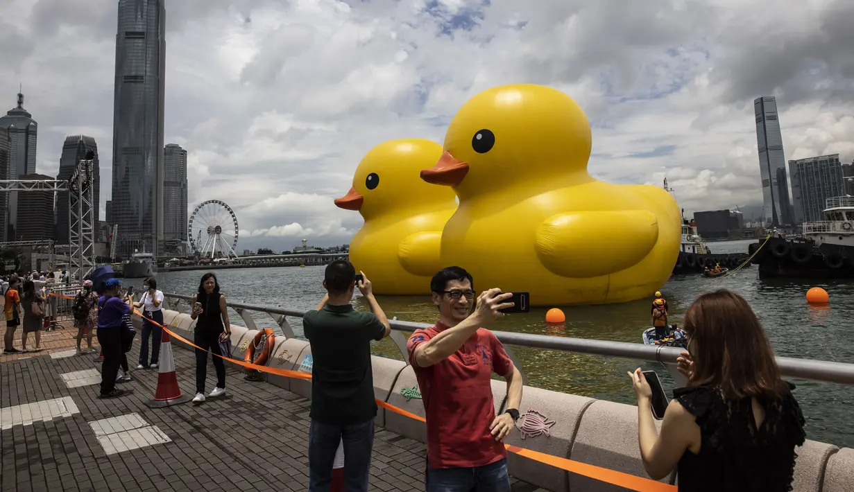 Tak lama setelah peluncurannya, puluhan warga dan turis berduyun-duyun ke kawasan pejalan kaki di dekat kantor pusat pemerintahan di Admiralty untuk mengambil foto bebek-bebek tersebut. (Photo by ISAAC LAWRENCE / AFP)