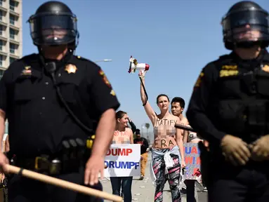 Petugas berjaga saat sejumlah wanita bertelanjang dada menolak Donald Trump di Burlingame, California (29/4). Demonstran menggelar aksi di depan Hotel Hyatt, lokasi Donald Trump melakukan kampanye Pilpres AS. (REUTERS/Noah Berger)