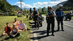 Polisi Prancis (kanan) berdiri di samping pengunjuk rasa lingkungan setelah aksi protes mereka menghentikan sementara balapan pada etape ke-10 Tour de France, antara Morzine dan Megeve, di Pegunungan Alpen Prancis, pada 12 Juli 2022. (AFP/Marco Bertorello)