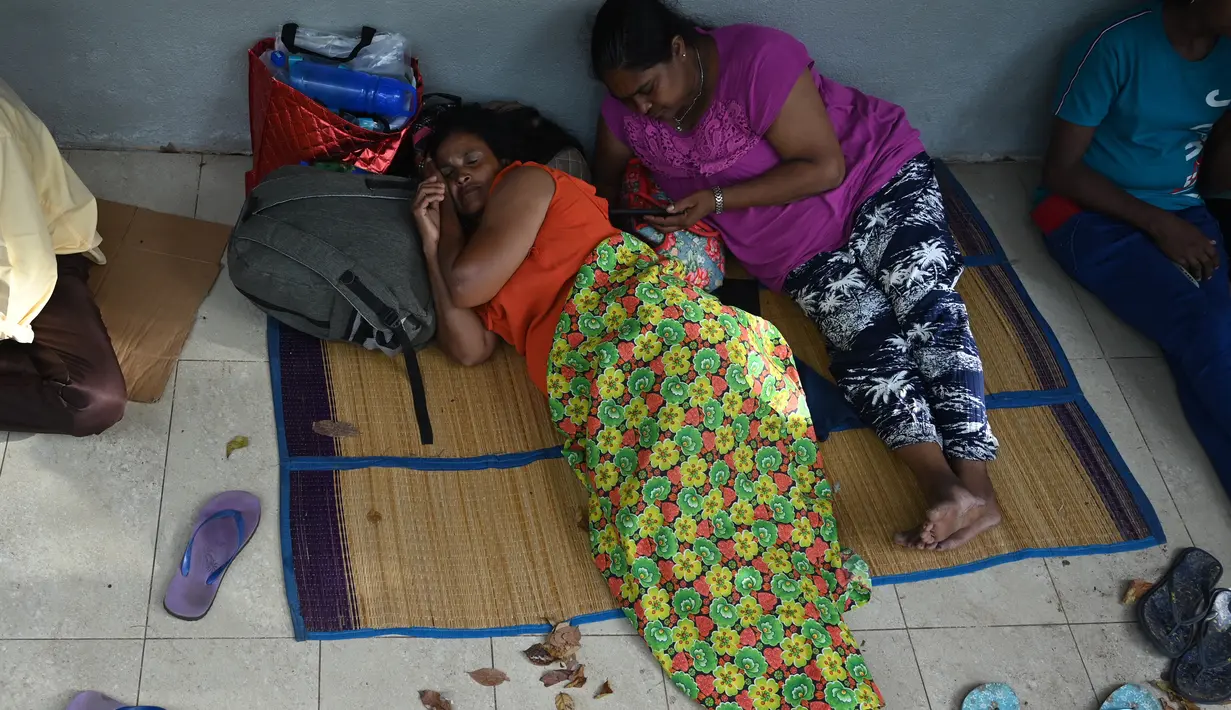 Dua perempuan berisitirahat saat menunggu depan kantor Imigrasi dan Emigrasi untuk mengurus paspor di Kolombo, Sri Lanka, Senin (18/7/2022). Negara kepulauan Samudra Hindia itu dilanda krisis ekonomi yang belum pernah terjadi sebelumnya yang telah memicu ketidakpastian politik. (Photo by Arun SANKAR / AFP)