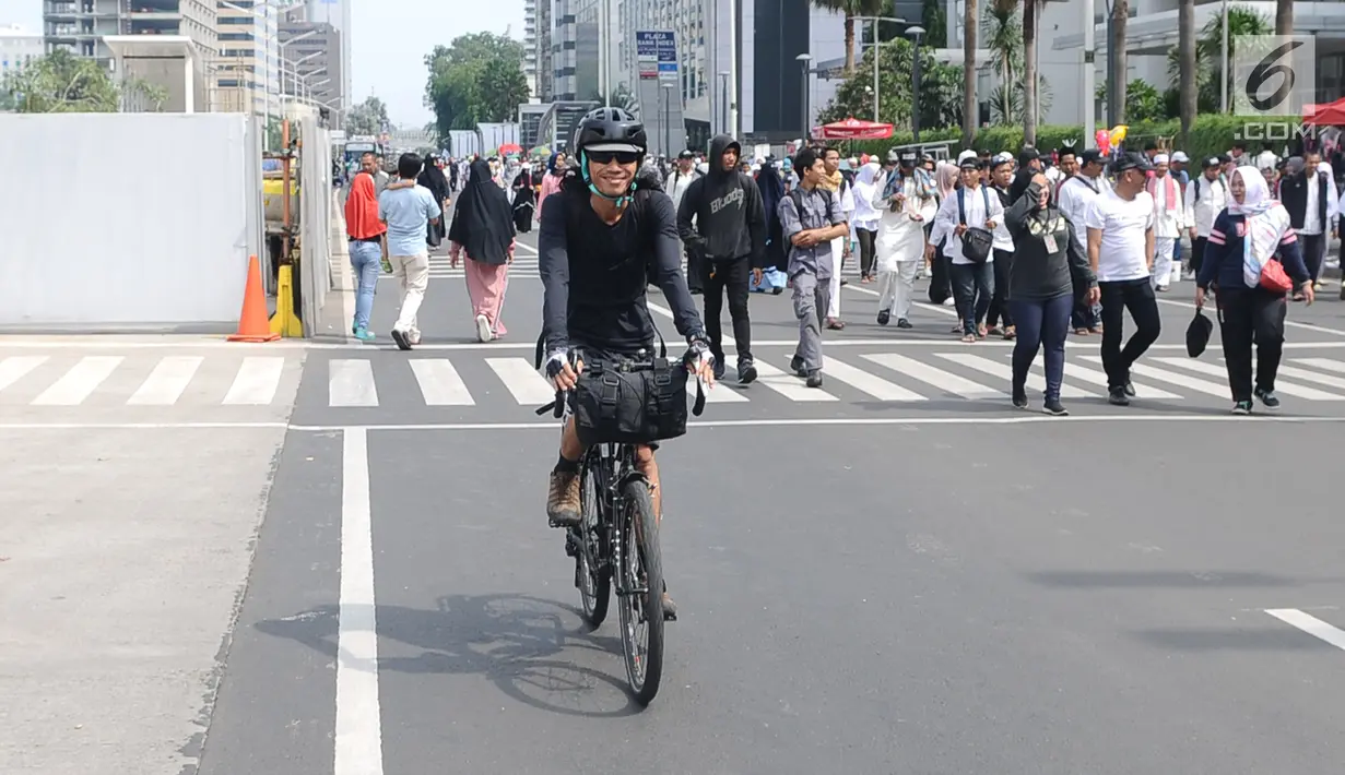 Seorang warga bersepeda di antara peserta Reuni 212 saat Car Free Day (CFD) di kawasan Jakarta, Minggu (2/12). Warga tetap memadati area Car Free Day  dari Bundaran HI-Sudirman meskipun ada aksi Reuni 212. (Liputan6.com/Angga Yuniar)