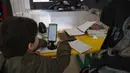 Banyak gedung sekolah di Lebanon dialihfungsikan menjadi pusat penampungan bagi warga yang mengungsi. Tampak dalam foto, seorang wanita Lebanon yang mengungsi duduk di samping seorang anak, mengawasi pelajaran daringnya melalui telepon seluler di sebuah sekolah negeri yang diubah menjadi tempat penampungan di kota Dekwaneh, utara Beirut, pada Rabu 25 Maret 2026. (Anwar AMRO/AFP)
