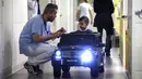 Petugas medis melihat Souvail (2) menggunakan mobil mainan listrik menuju ruang operasi di Rumah Sakit Valenciennes, Prancis, Jumat (2/2). Program ini untuk membuat anak-anak lebih santai sebelum menjalani prosedur operasi. (FRANCOIS LO PRESTI/AFP)