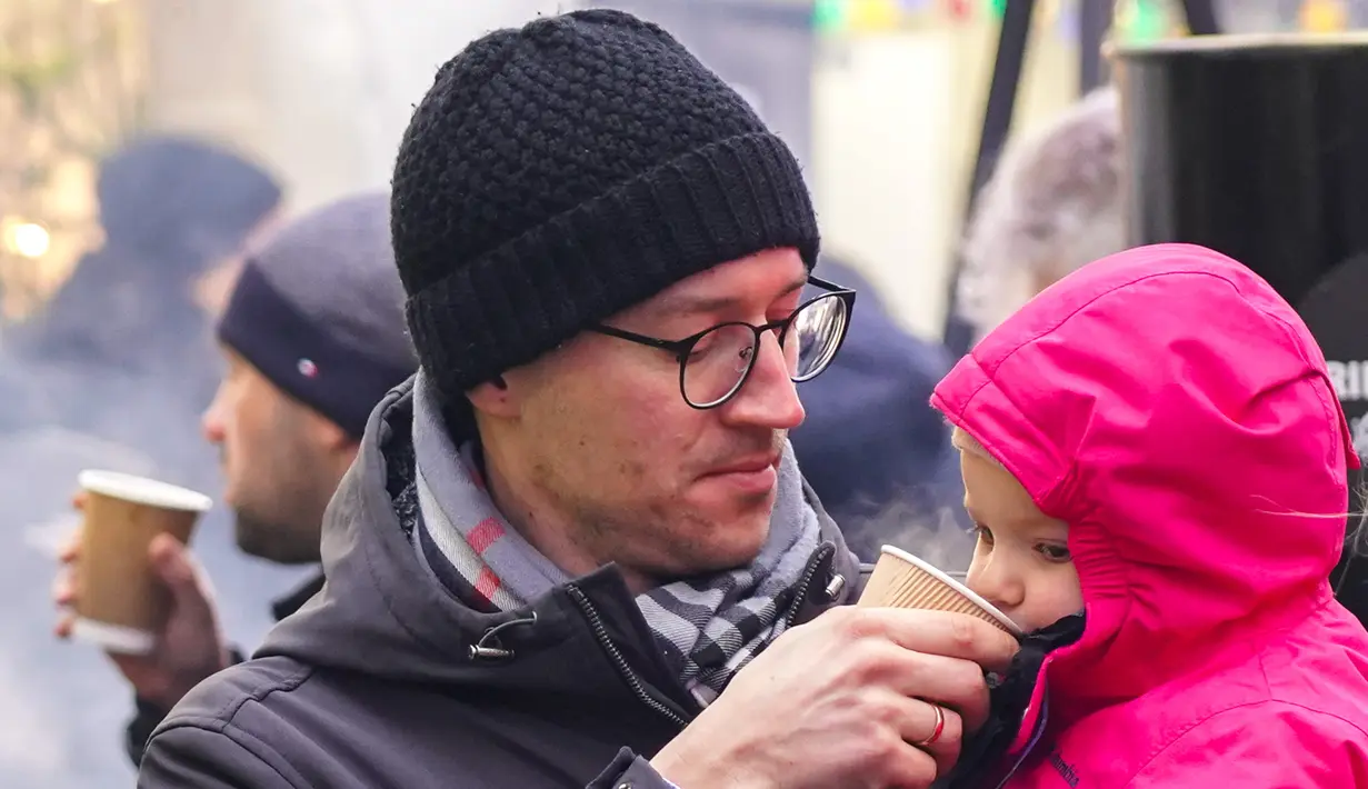 Pengunjung memberi minum anak perempuannya saat Riga Street Food Festival di Riga, Latvia, Sabtu (18/1/2020). Api unggun dan kios-kios makanan didirikan di sudut Jalan Kalku dan Valnu di Kota Tua Riga agar orang-orang dapat menikmati berbagai hidangan populer dari kota tersebut. (Xinhua/Janis)