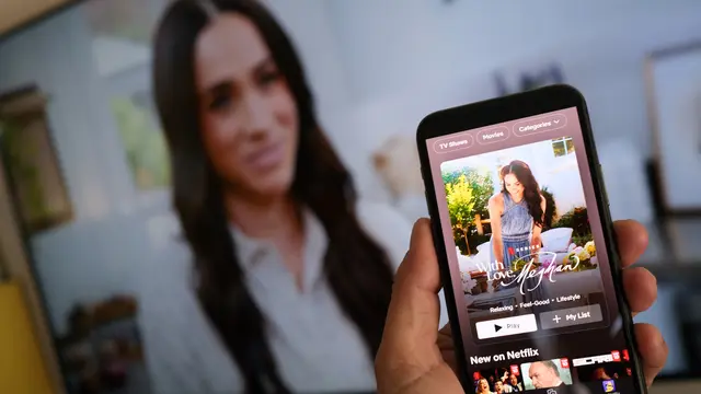 Seseorang memegang telepon pintar yang menampilkan acara baru Meghan Markle di Netflix, “With Love, Meghan”, di depan layar TV yang menayangkan cuplikan acara tersebut, di Los Angeles, 4 Maret 2025.