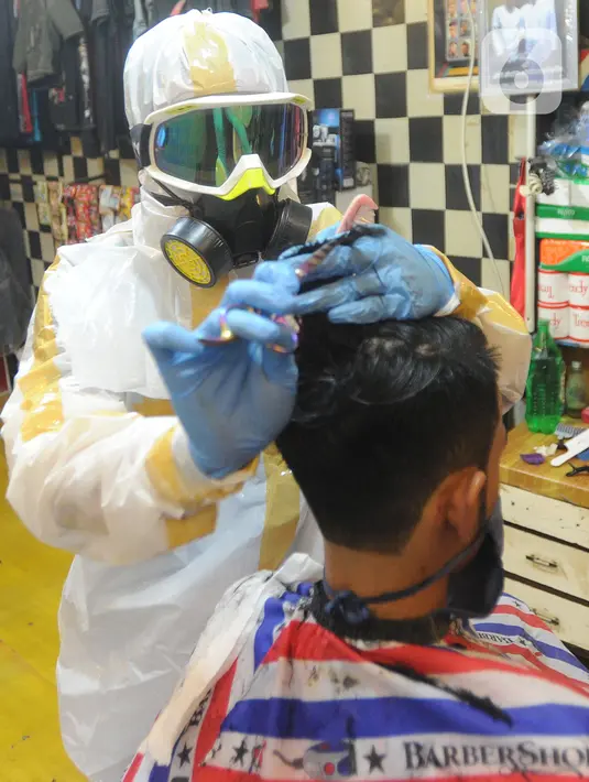 Seorang tukang cukur mengenakan alat pelindung diri (APD) saat memangkas rambut pelanggannya di Chemot Barbershop, Ciawi, Bogor, Jawa Barat, Minggu (5/4/2020). Penggunaan APD tersebut sebagai antisipasi agar lebih waspada terhadap penularan virus corona Covid-19. (merdeka.com/Arie Basuki)