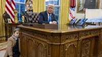 Presiden AS Donald Trump duduk di belakang meja Resolute di Ruang Oval, Gedung Putih, saat anak Elon Musk ikut hadir bersama bapaknya pada Selasa, 11 Februari 2025. (dok. Jim Watson/AFP)