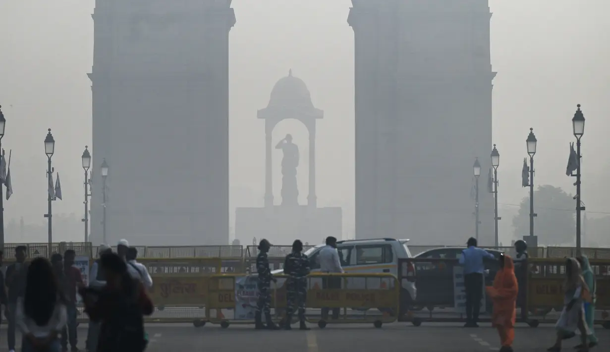 Pejalan kaki berjalan di sepanjang jalan dekat Gerbang India di tengah kabut asap tebal di New Delhi, Kamis (3/11/2022). Setiap musim dingin, udara dingin beserta asap dari petani yang membakar jerami dan emisi kendaraan juga sumber-sumber lainnya bercampur menciptakan kabut asap mematikan. (Money SHARMA / AFP)