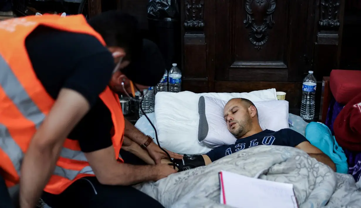 Relawan paramedis merawat seorang migran yang mogok makan saat ia menduduki Gereja Saint-Jean-Baptiste-au-Beguinage di Brussel, Belgia, Rabu (2/6/2021). Para migran menyerukan lebih banyak inisiatif untuk memungkinkan mereka bekerja.
(Kenzo TRIBOUILLARD/AFP)