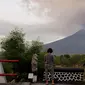 Wisatawan melihat asap Gunung Agung di sebuah kuil di Kabupaten Karangasem, Bali, (27/11). Pihak berwenang telah mengantisipasi dampak yang ditimbulkan oleh aktivitas Gunung Agung dengan menutup Bandara Ngurah Rai. (AP Photo / Firdia Lisnawati)