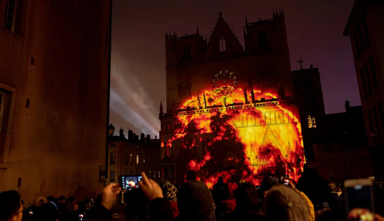Orang-orang mengambil gambar Katedral Saint-Jean-Baptiste ketika diterangi cahaya lampu selama Festival of Lights (Fete des Lumieres) di kota Lyon, Prancis, Kamis (5/12/2019). Festival yang digelar sejak tahun 1852 ini berlangsung, bertepatan dengan musim liburan Natal. (ROMAIN LAFABREGUE / AFP)