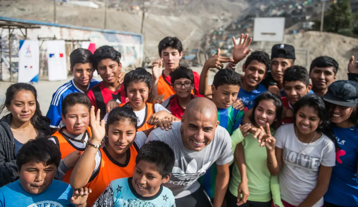 Mantan pemain bola Juventus, David Trezeguet berfoto bersama anak-anak di komunitas San Pablo Mirador, Peru (13/7). Trezeguet melakukan kunjungan ke Peru untuk mempromosikan Paris yang menjadi tuan rumah Olimpiade 2024. (AFP Photo/Ernesto Benavides)