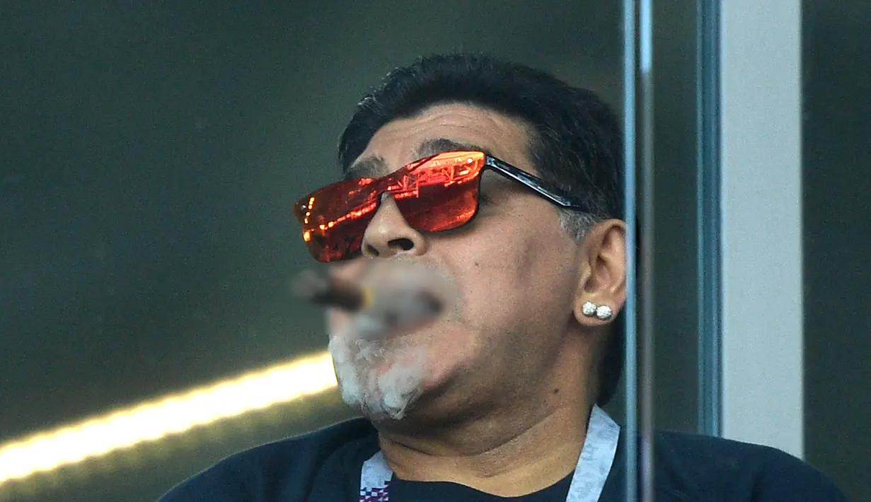 Mantan bintang sepak bola, Diego Maradona merokok saat menyaksikan laga antara Argentina dan Islandia dalam penyisihan Grup D Piala Dunia 2018 di Stadion Spartak, Moskow, Rusia, Sabtu (16/6). (Juan Mabromata/AFP)