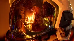 Falla terbakar saat tercermin dalam helm pemadam kebakaran selama festival Fallas tradisional di Valencia (19/3/2022). Fallas adalah struktur raksasa yang terbuat dari karton yang menggambarkan peristiwa dan kepribadian terkini di mana tokoh individu atau Ninot ditempatkan. (AP Photo/Alberto Saiz)