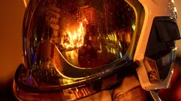 Falla terbakar saat tercermin dalam helm pemadam kebakaran selama festival Fallas tradisional di Valencia (19/3/2022). Fallas adalah struktur raksasa yang terbuat dari karton yang menggambarkan peristiwa dan kepribadian terkini di mana tokoh individu atau Ninot ditempatkan. (AP Photo/Alberto Saiz)