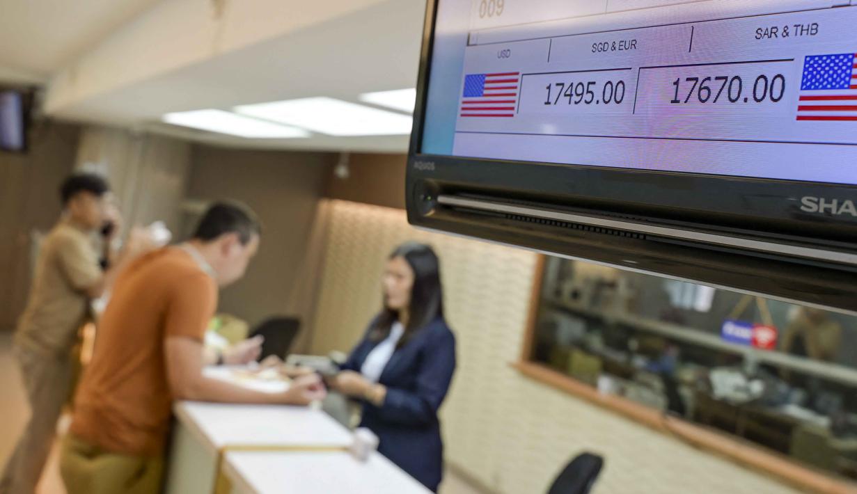 Tekanan terhadap rupiah terjadi di tengah meningkatnya ketidakpastian global, termasuk sentimen suku bunga tinggi di Amerika Serikat serta kekhawatiran pasar terhadap dinamika geopolitik internasional. Tampak dalam foto, sebuah monitor menampilkan kurs jual dan beli Rupiah terhadap Dolar AS, saat seorang penukar uang melayani pelanggan (belakang) di Jakarta pada 12 Mei 2026. (BAY ISMOYO/AFP)