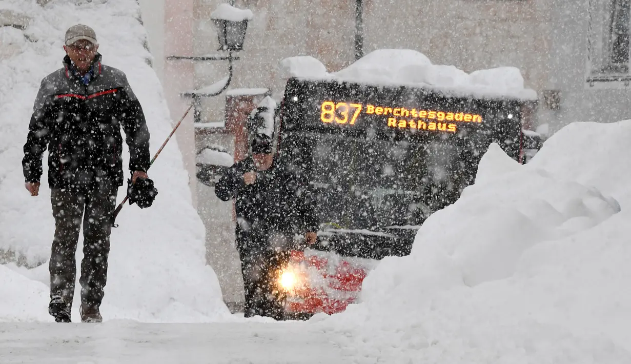 Seorang pria dan sebuah bus mencoba berjalan di jalan yang tertutup salju tebal di Berchtesgaden, Jerman, Kamis (10/1). (Tobias Hase/dpa/AFP)