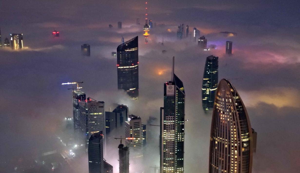 Suhu dingin dan kelembapan tinggi selama malam dan dini hari menciptakan kondisi ideal untuk terbentuknya kabut. Tampak foto udara memperlihatkan gedung pencakar langit yang tertutup kabut pagi di Kota Kuwait pada Minggu 9 November 2025. (YASSER AL-ZAYYAT/AFP)