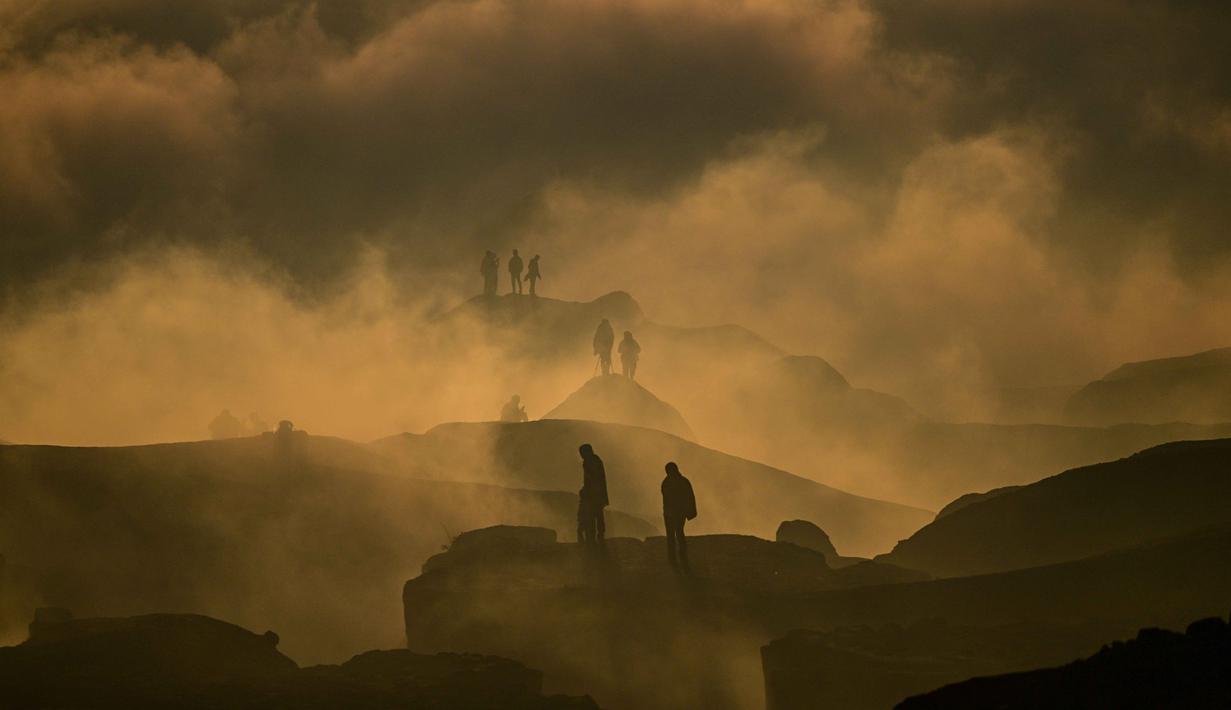 Para penganut Hindu dari komunitas Tengger terlihat melalui awan rendah saat matahari terbit ketika mereka mendaki gunung berapi aktif Bromo untuk mempersembahkan sesaji berupa beras, buah-buahan, ternak, dan barang-barang lainnya sebagai bagian dari festival Yadnya Kasada di Probolinggo, Jawa Timur, Senin 1 Juni 2026. (JUNI KRISWANTO/AFP)
